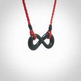 This piece is a fine, delicate eternity shaped pendant. It was carved from a lovely dark piece of black jade. It is suspended on an red braided cord that is length adjustable.